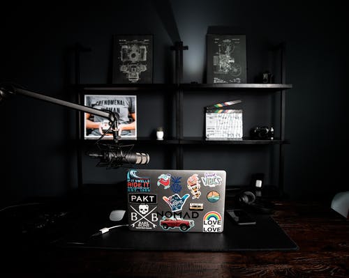 Laptop with bright stickers near shelf with decorative frames