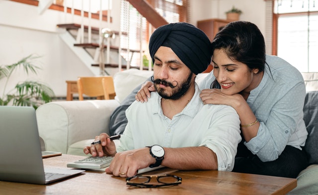cheerful south asian couple using calculator while sitting at table