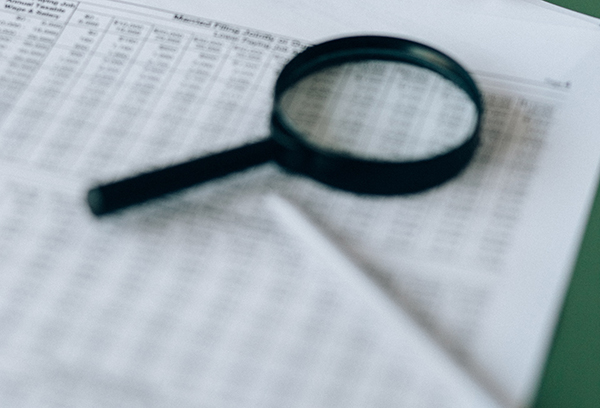 magnifying glass and pen on top of paper with chart